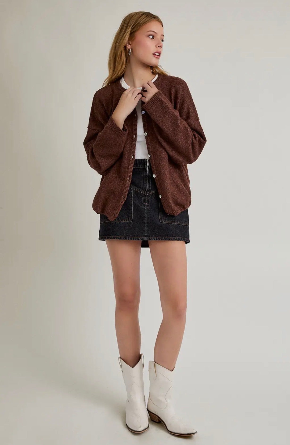 Woman wearing a brown jacket, black skirt, and white boots on a plain background